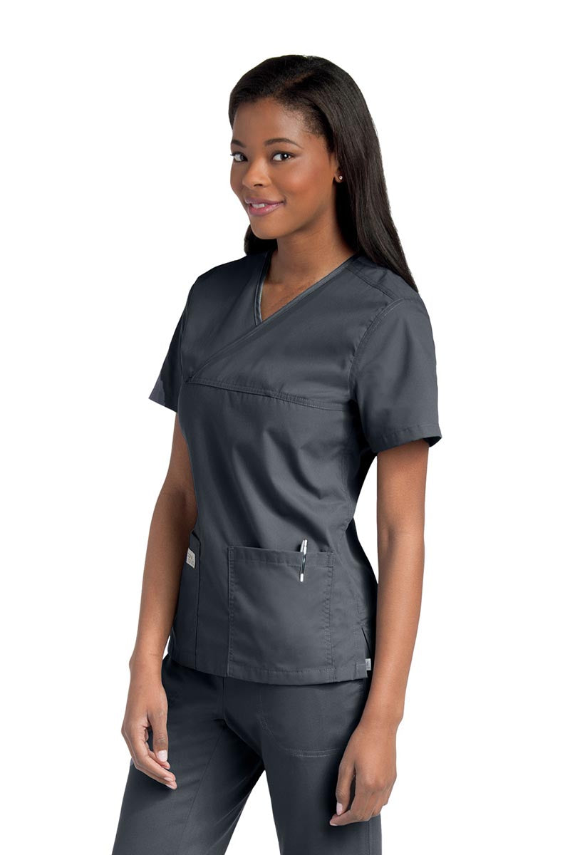 Female nurse wearing an Urbane Essentials Women's Crossover Scrub Top in "Graphite" featuring 2 front patch pockets.