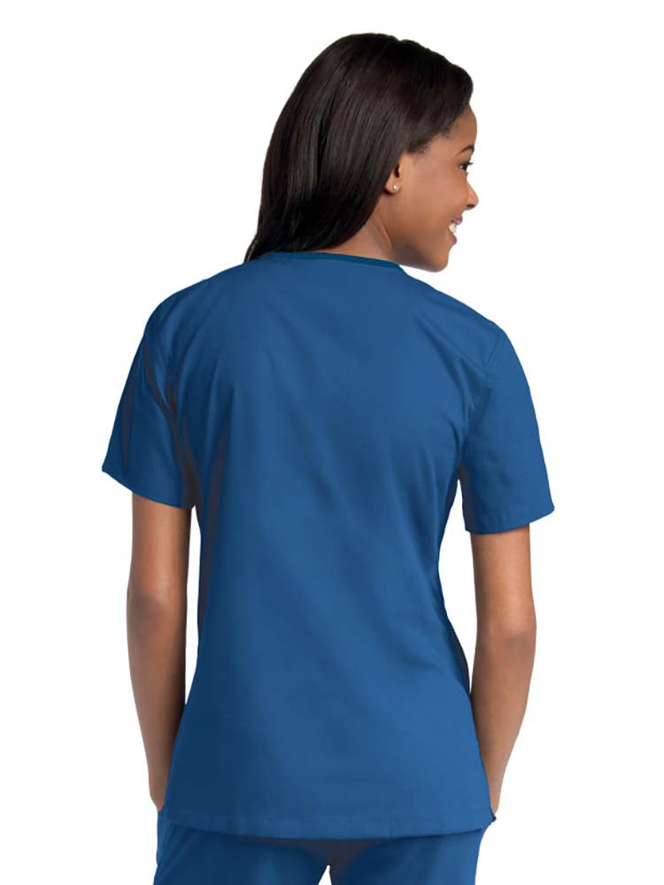 Young female healthcare worker wearing an Urbane Essentials Women's Crossover Scrub Top in "Galaxy Blue" featuring side vents for increased range of motion.