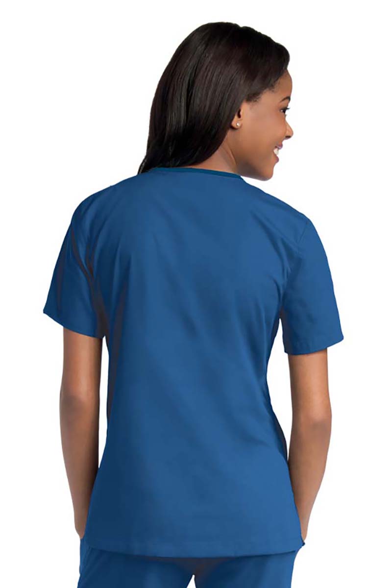 Young female healthcare worker wearing an Urbane Essentials Women's Crossover Scrub Top in "Royal Blue" featuring side vents for increased range of motion.