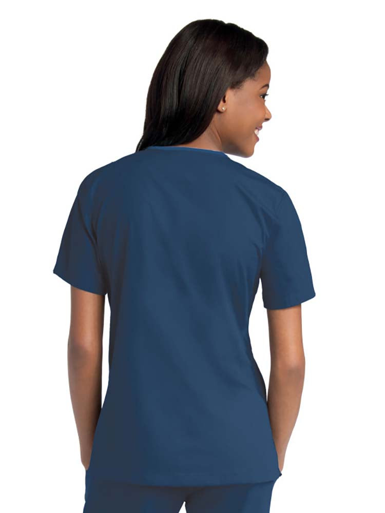 Young female healthcare worker wearing an Urbane Essentials Women's Crossover Scrub Top in "Navy" featuring side vents for increased range of motion.