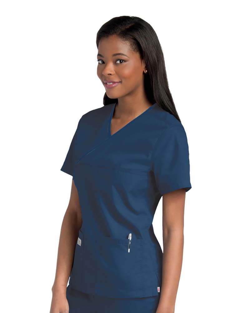 Female nurse wearing an Urbane Essentials Women's Crossover Scrub Top in "Navy" featuring 2 front patch pockets.