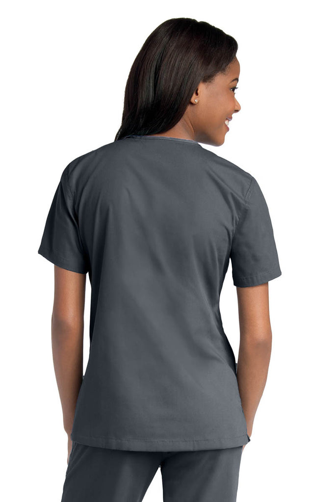 Young female healthcare worker wearing an Urbane Essentials Women's Crossover Scrub Top in "Steel Grey" featuring side vents for increased range of motion.