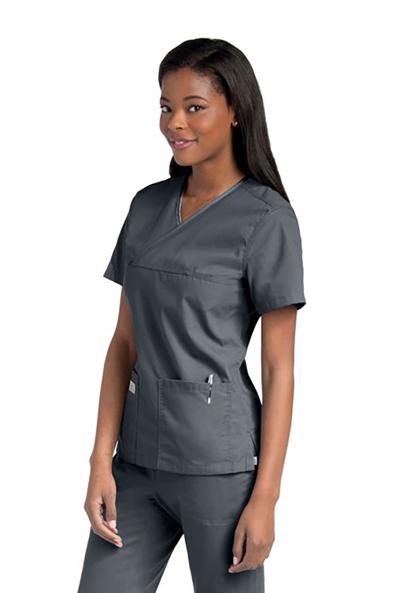 Female nurse wearing an Urbane Essentials Women's Crossover Scrub Top in "Steel Grey" featuring 2 front patch pockets.