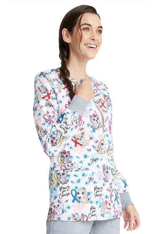 A female RN wearing a Cherokee Women's Snap Front Print Scrub Jacket in "Paws for a Cause" featuring 2 front pockets for all of your on-the-go storage needs.