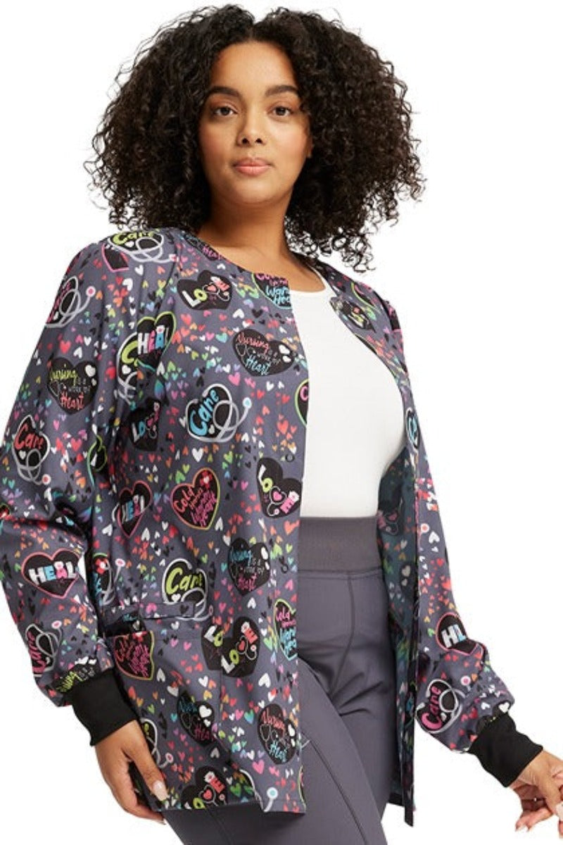 A young LPN wearing a Cherokee Women's Print Snap Front Jacket in "Work of Heart" featuring 2 front patch pockets for all of your on the go storage needs.