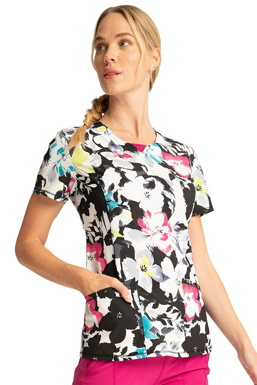 A female LPN wearing a Cherokee Infinity Women's Round Neck Print Top in "Inky Garden" featuring 2 front patch pockets.