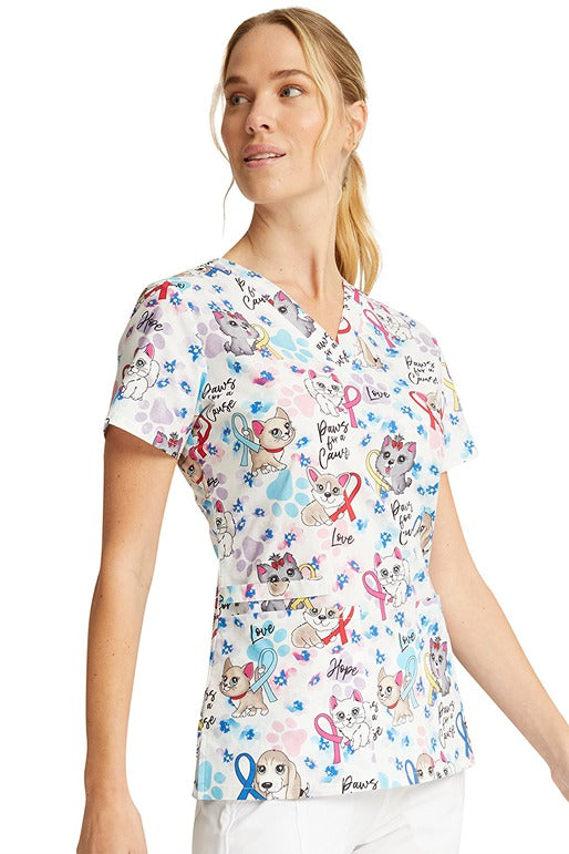 A young woman wearing a Cherokee Women's V-Neck Print Scrub Top in "Paws for a Cause" featuring v-neckline & short sleeves. 