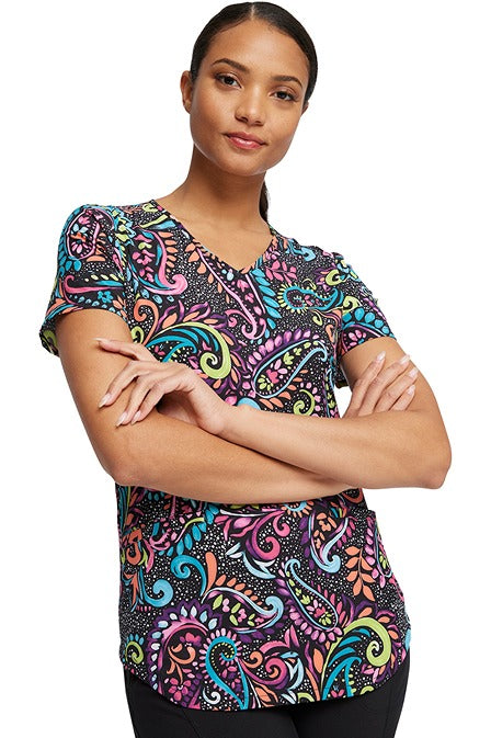 A young female LPN wearing a Women's V-Neck Print Scrub Top from Cherokee Uniforms in "Painted Paisley" featuring a banded V-neckline.