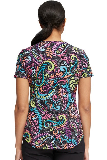 A young female nurse wearing a Cherokee Women's V-Neck Print Scrub Top in "Painted Paisley" featuring a center back length of 28.5".