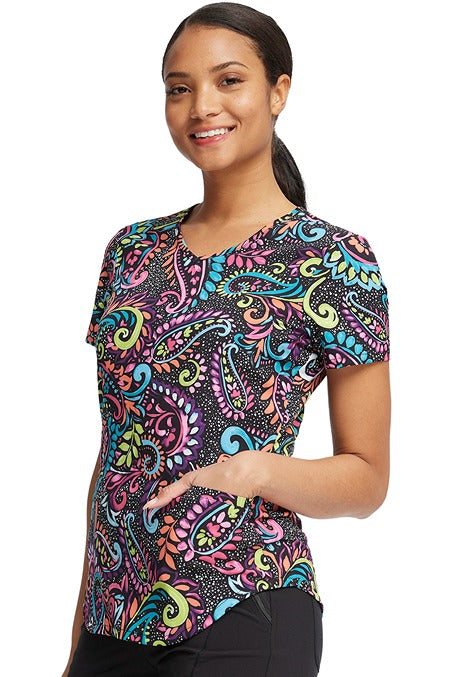 A young Home Care Registered Nurse wearing a Cherokee Women's V-Neck Print Scrub Top in "Painted Paisley" featuring a curved hemline & side vents to ensure a flattering all day look.