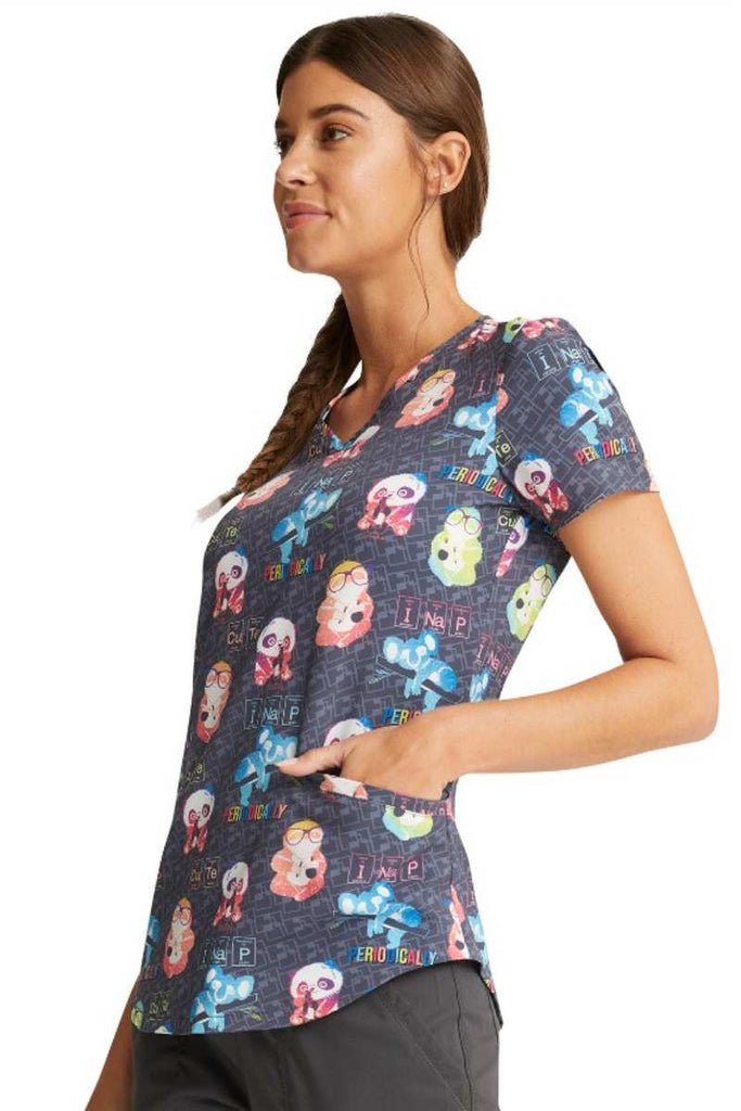 A young female Helathcare worker wearing a Cherokee Women's V-neck print Scrub Top in "Science Friends" featuring 2 front welt pockets.