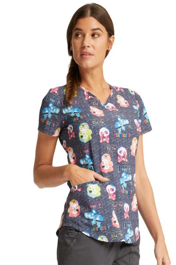 A young female Medical Assistant wearing a Cherokee Women's V-neck Print Scrub Top in "Science Friends" featuring a curved hem.