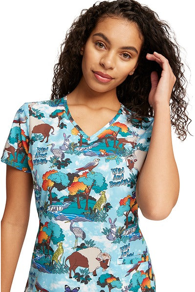 A young nurse wearing a Women's V-Neck Print Scrub Top from Cherokee Uniforms in "Wildlife Sanctuary" size XS featuring a modern classic fit. 