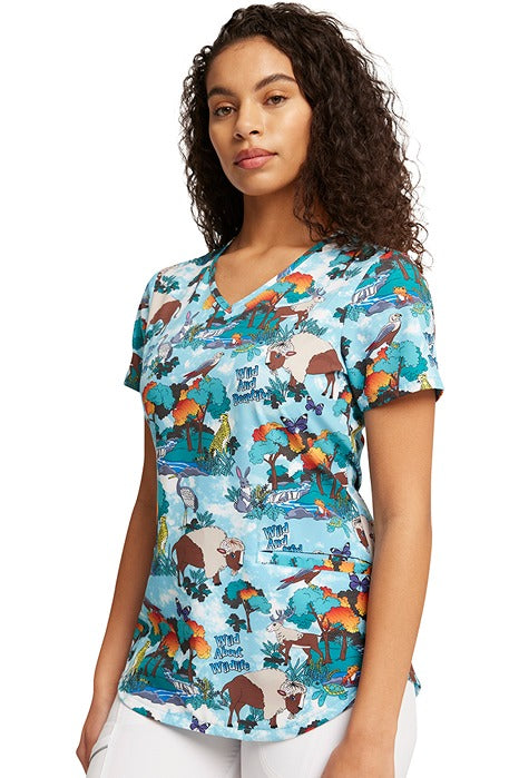 A young woman wearing a Women's V-Neck Print Scrub Top from Cherokee in "Wildlife Sanctuary" size XL featuring a curved hem.