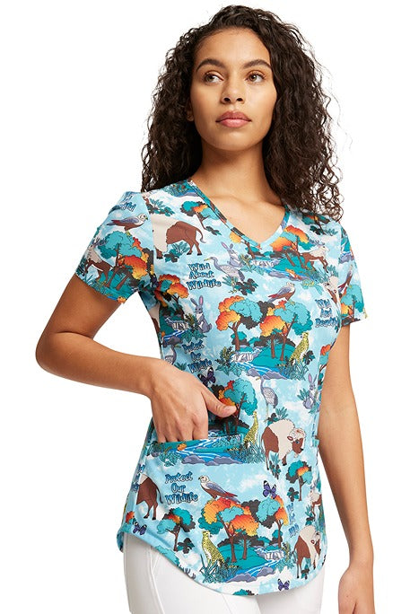 A female LPN wearing a Cherokee Women's V-Neck Print Scrub Top in "Wildlife Sanctuary" size small featuring short sleeves & a v-neckline.