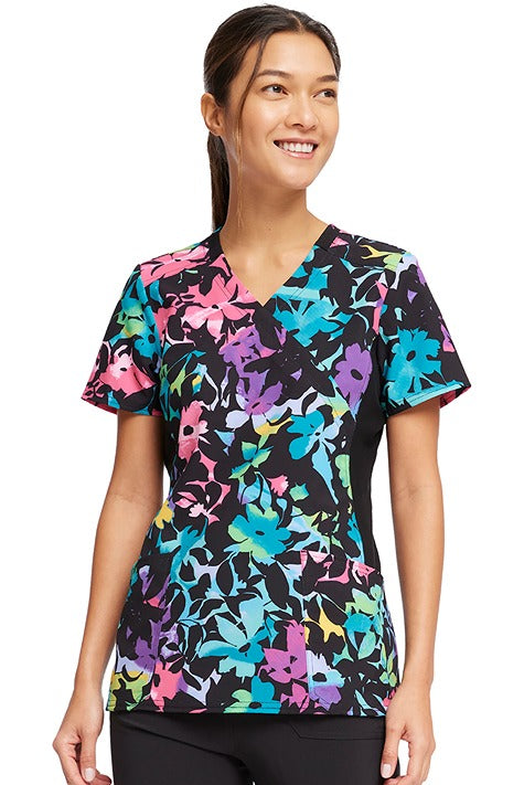 A young female Home Care Registered Nurse wearing a Cherokee Women's Knit Panel Print Top in "Rainbow Fleurs" featuring front princess seaming to ensure a flattering fit.