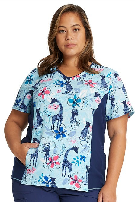A young female Physician's Assistant wearing a Cherokee Women's V-neck Print Scrub Top in "Jungle Blues" size 2XL featuring side stretch panels.