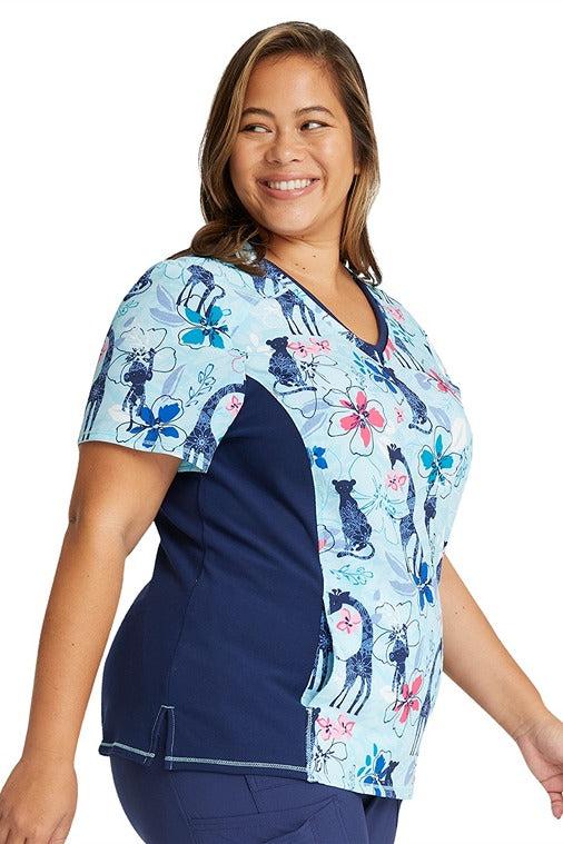 A young female Medical Assistant wearing a Cherokee Women's V-neck Print Scrub Top in "Jungle Blues" featuring Side slits for additional mobility.