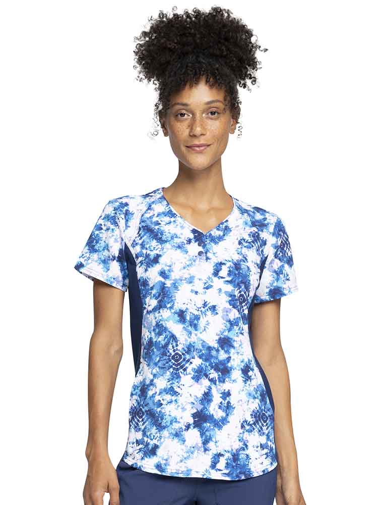 A young female healthcare professional wearing a Cherokee iFlex Women's V-Neck Print Top in Tranquil Tie Dye featuring front shoulder yokes for a distinct & flattering look.