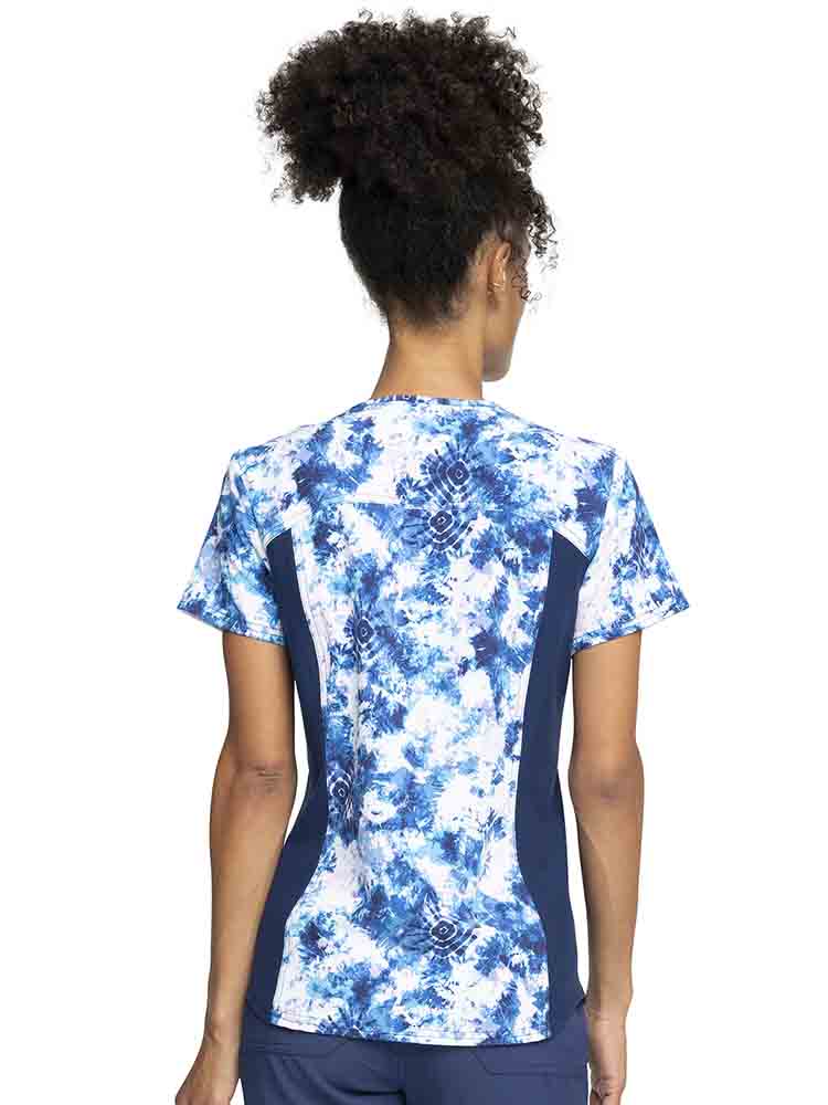 Young woman wearing a Cherokee iFlex Women's V-Neck Print Top in Tranquil Tie Dye featuring 2 side knit panels to provide additional range of motion & a comfortable all day fit.