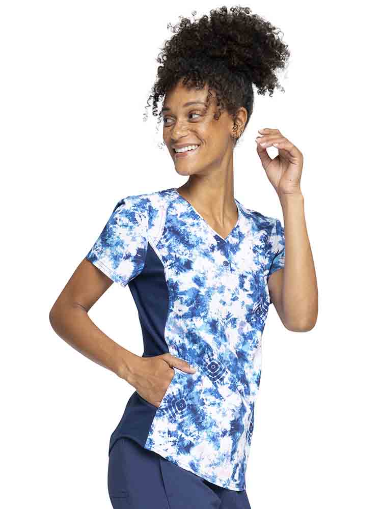 Female nurse wearing a Cherokee iFlex Women's V-Neck Print Top in Tranquil Tie Dye featuring 2 inseam, slash pockets for all of your on the go storage needs.