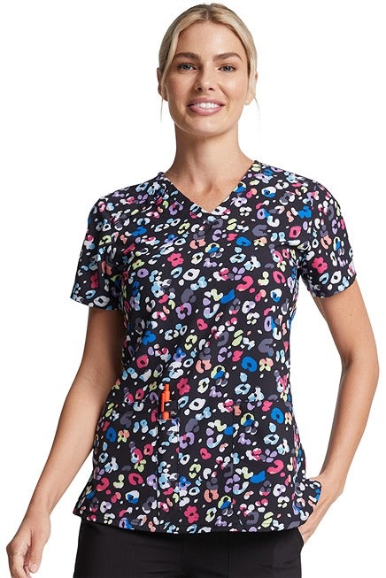 A young woman wearing a Women's V-Neck Print Scrub Top from Dickies Medical in "Safari Pop" featuring a contemporary fit.