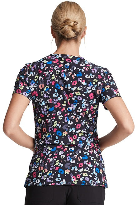 A young female CNA wearing a Dickies Women's V-Neck Print Scrub Top in "Safari Pop" featuring back princess seaming to ensure a flattering look.