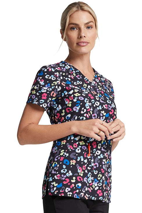A young female RN wearing a Dickies Women's V-Neck Print Scrub Top in "Safari Pop" featuring a center back length of 26".