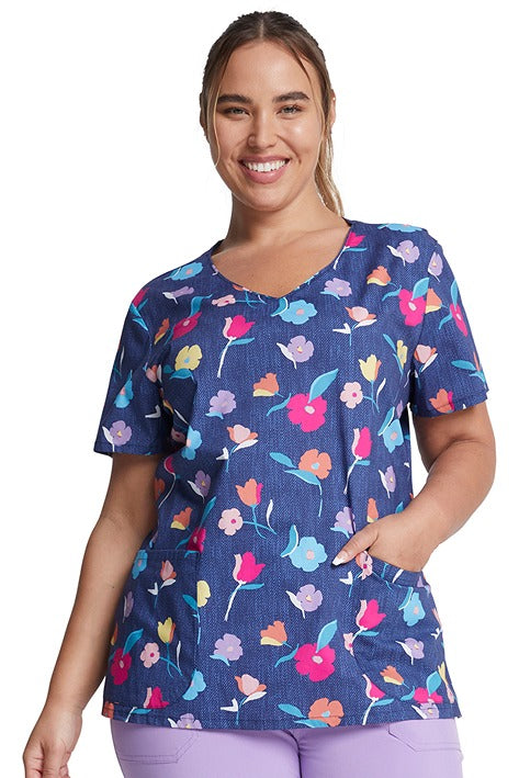 A young woman wearing a Women's V-Neck Print Scrub Top from Dickies Medical in "Denim Garden" featuring a contemporary fit.