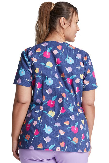 A female CNA wearing a Dickies Women's V-Neck Print Scrub Top in "Denim Garden" featuring back darts for shaping.