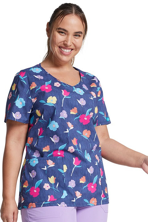 A young woman wearing a Dickies Women's V-Neck Print Scrub Top in "Denim Garden" featuring 2 front patch pockets.
