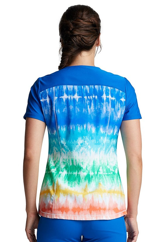 An image showing the back of a young female Family Practitioner wearing the Cherokee Women's V-neck Print Scrub Top in "Rainbow Stripes" size medium featuring a center back length of 26".