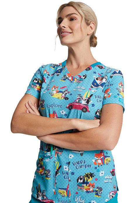A young Registered Nurse wearing a Dickies Women's V-neck Print Scrub Top in "Vacay All Day" featuring bust darts for shaping & side vents for ease of movement.