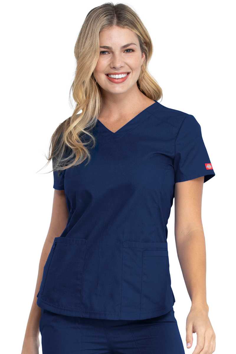 A young female Medical Assistant wearing a Dickies Women's V-Neck Scrub Top in Navy size Small featuring a total of 4 pockets.