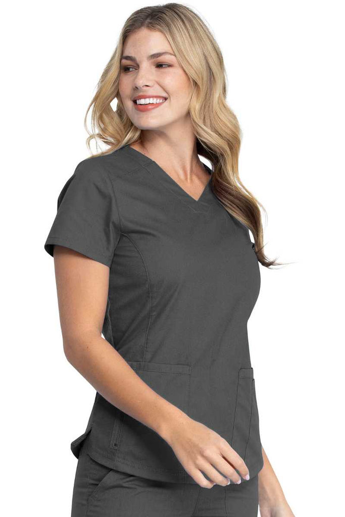 A young female LPN wearing a Dickies EDS Signature Women's V-neck Scrub Top in Pewter size Large featuring princess seaming throughout the front.
