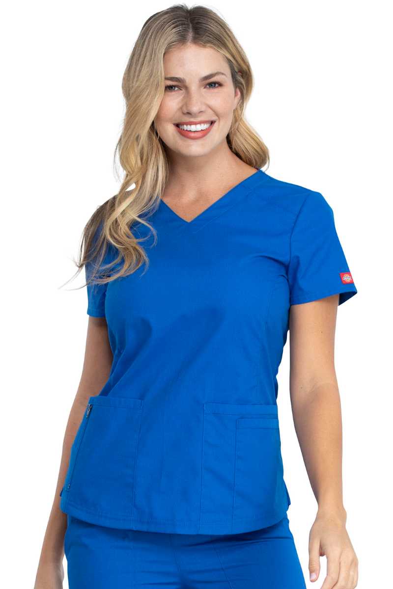 A young female Medical Assistant wearing a Dickies Women's V-Neck Scrub Top in Royal size Medium featuring a total of 4 pockets.