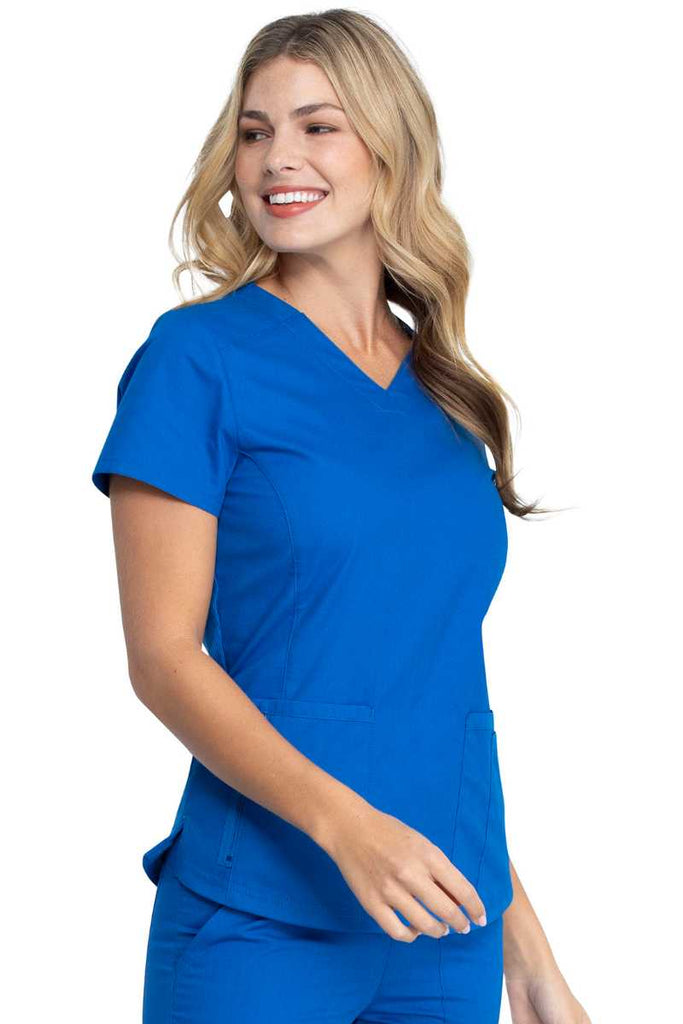 A young female LPN wearing a Dickies EDS Signature Women's V-neck Scrub Top in Royal size Large featuring princess seaming throughout the front.