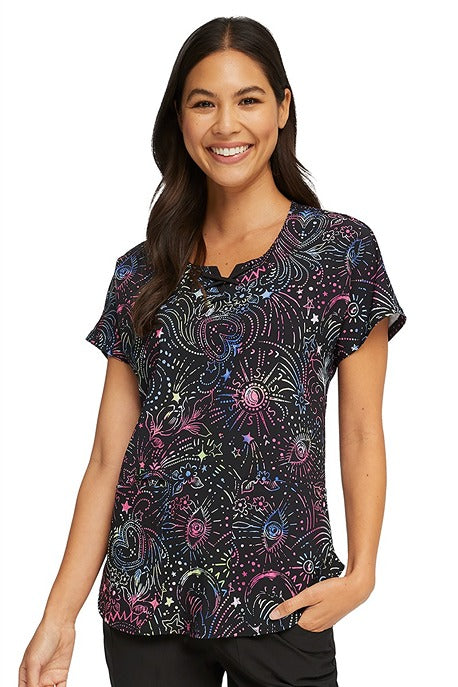 A young female Phlebotomist wearing a HeartSoul Women's Round Neck Print Scrub Top in "Celestial Twist" featuring a stylish rounded neckline & short sleeves. 