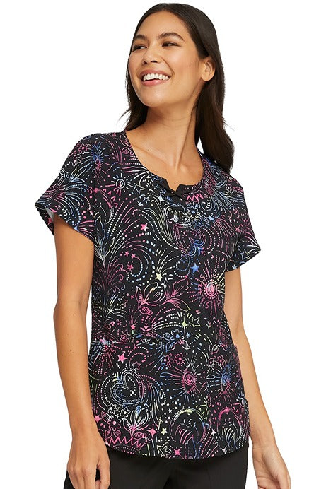 A young female Healthcare Professional wearing a HeartSou; Women's Round Neck Print Scrub Top In "Celestial Twist " size XS featuring doub;e needle topstitching throughout for shaping & a flattering fit.
