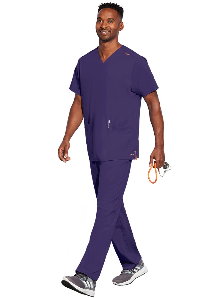 Young male LPN wearing a Unisex V-Neck Scrub Top from Barco Motion in New Grape size Small featuring a total of 5 pockets for all of your daily storage needs.