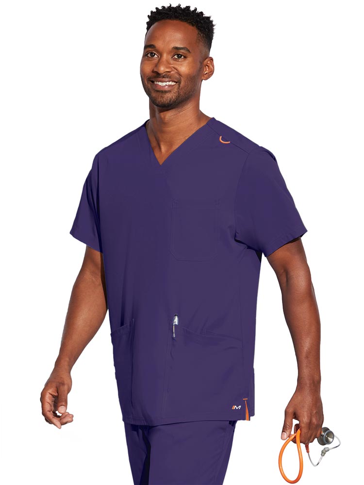 A young male CNA wearing a Barco Motion Unisex V-Neck Scrub Top in New Grape size 2XL featuring a V-neckline with lap over styling.
