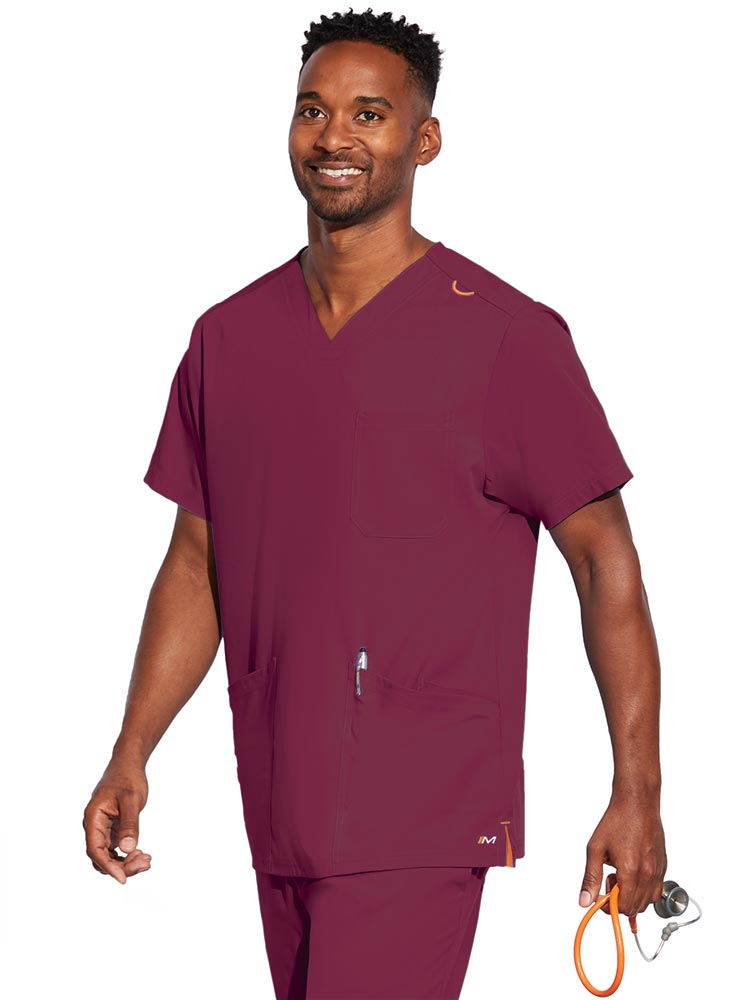 A young male CNA wearing a Barco Motion Unisex V-Neck Scrub Top in Wine size Large featuring a V-neckline with lap over styling.