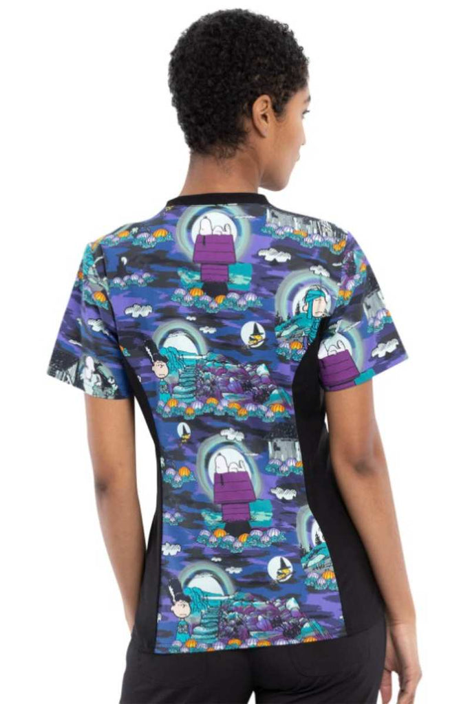 A young female Pediatrician wearing a Tooniforms Women's V-neck Knit Panel Print Top in Midnight Pumpkin featuring a medium center back length of 26".