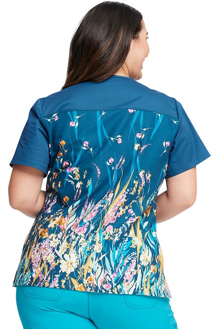 A young Home Care Registered Nurse wearing a Tooniforms Women's V-Neck Print Top in "Flower Walk" featuring a front angled shoulder yoke & back contrast yoke to ensure a comfortable & stylish all day fit.