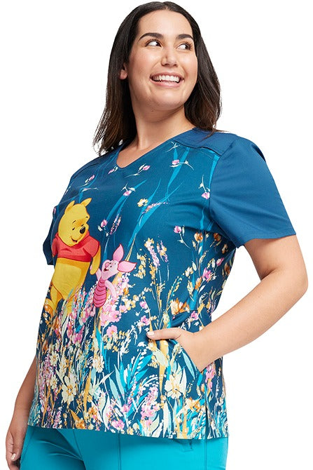 A female LPN wearing a Tooniforms Women's V-Neck Print Top in "Flower Walk" featuring 2 side angled pockets for all of your on the go storage needs.