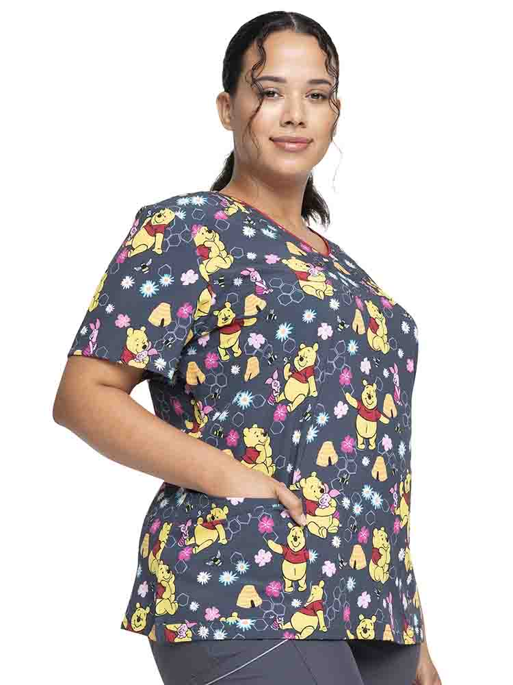 Young woman wearing a Tooniforms Women's V-Neck Print Scrub Top in "Bee's Knees" featuring 2 front patch pockets for your on the go storage needs.  