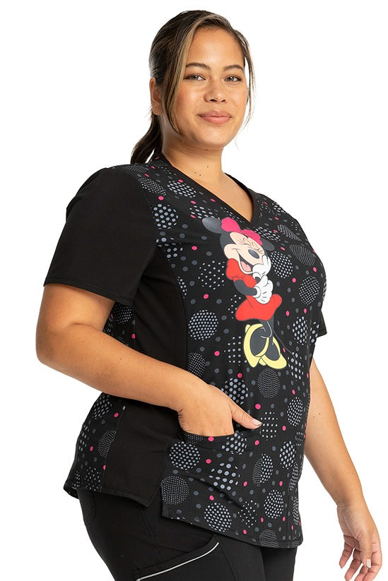 A young female LPN wearing a Tooniforms Women's Stylized V-Neck Print Top in "Minnie Spotlight" featuring front & back princess seaming to ensure a flattering fit.