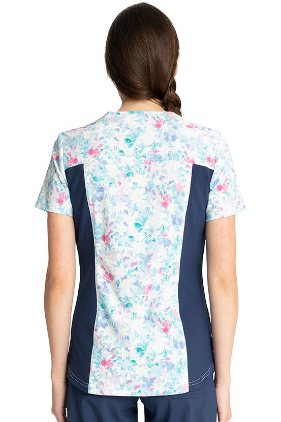 A female Registered Nurse wearing a Tooniforms Women's V-Neck Print Top in "Find Joy" featuring contrast side panels & side vents. 