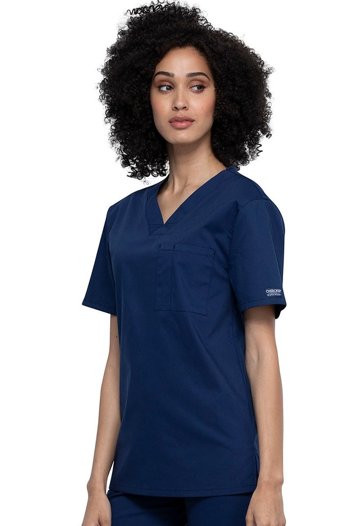 A picture of a young female Helathcare Professional wearing a Cherokee Unisex Tuckable V-neck Scrub Top in Navy size Small featuring side slits for additional range of motion