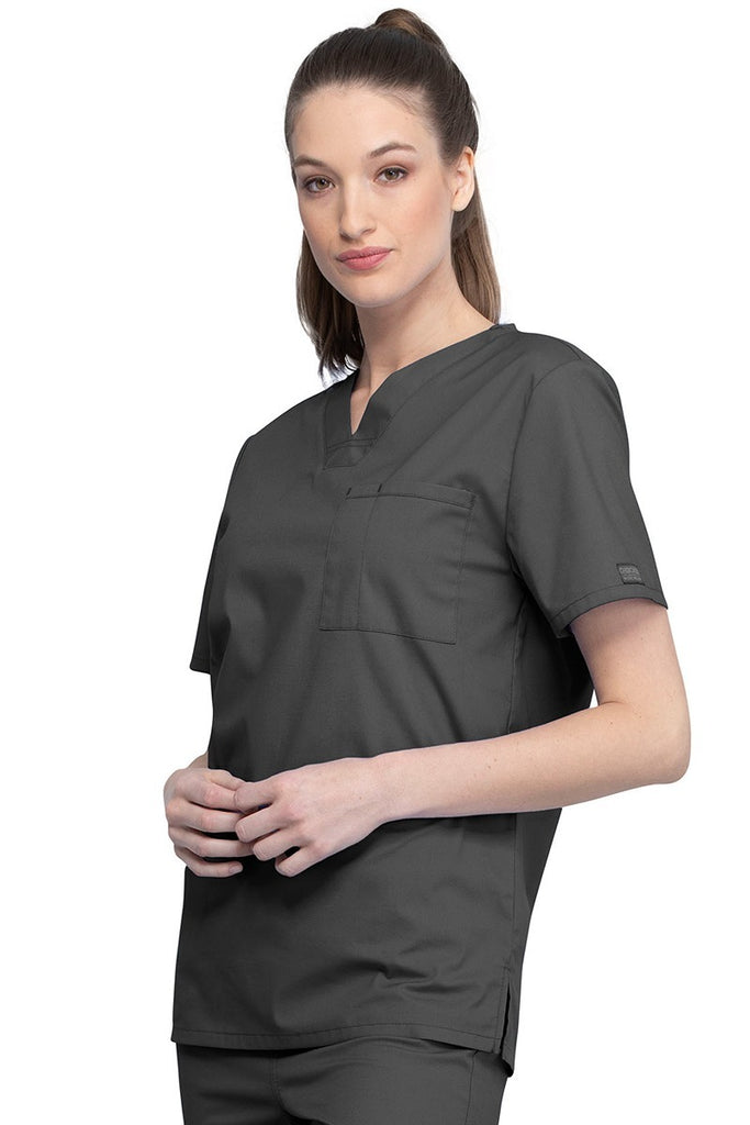 A picture of a young female Helathcare Professional wearing a Cherokee Unisex Tuckable V-neck Scrub Top in Pewter size Small featuring side slits for additional range of motion